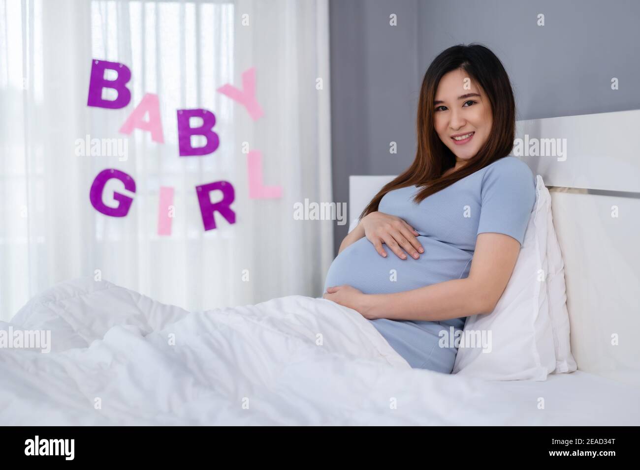 pregnant woman stroking her belly on a bed with baby girl sign Stock Photo
