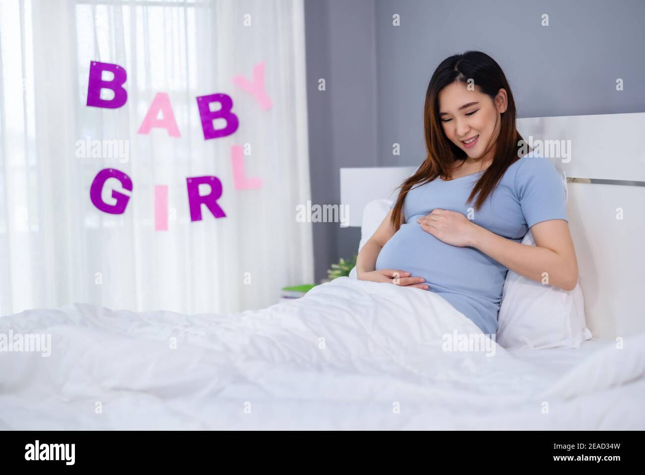 pregnant woman stroking her belly on a bed with baby girl sign Stock Photo