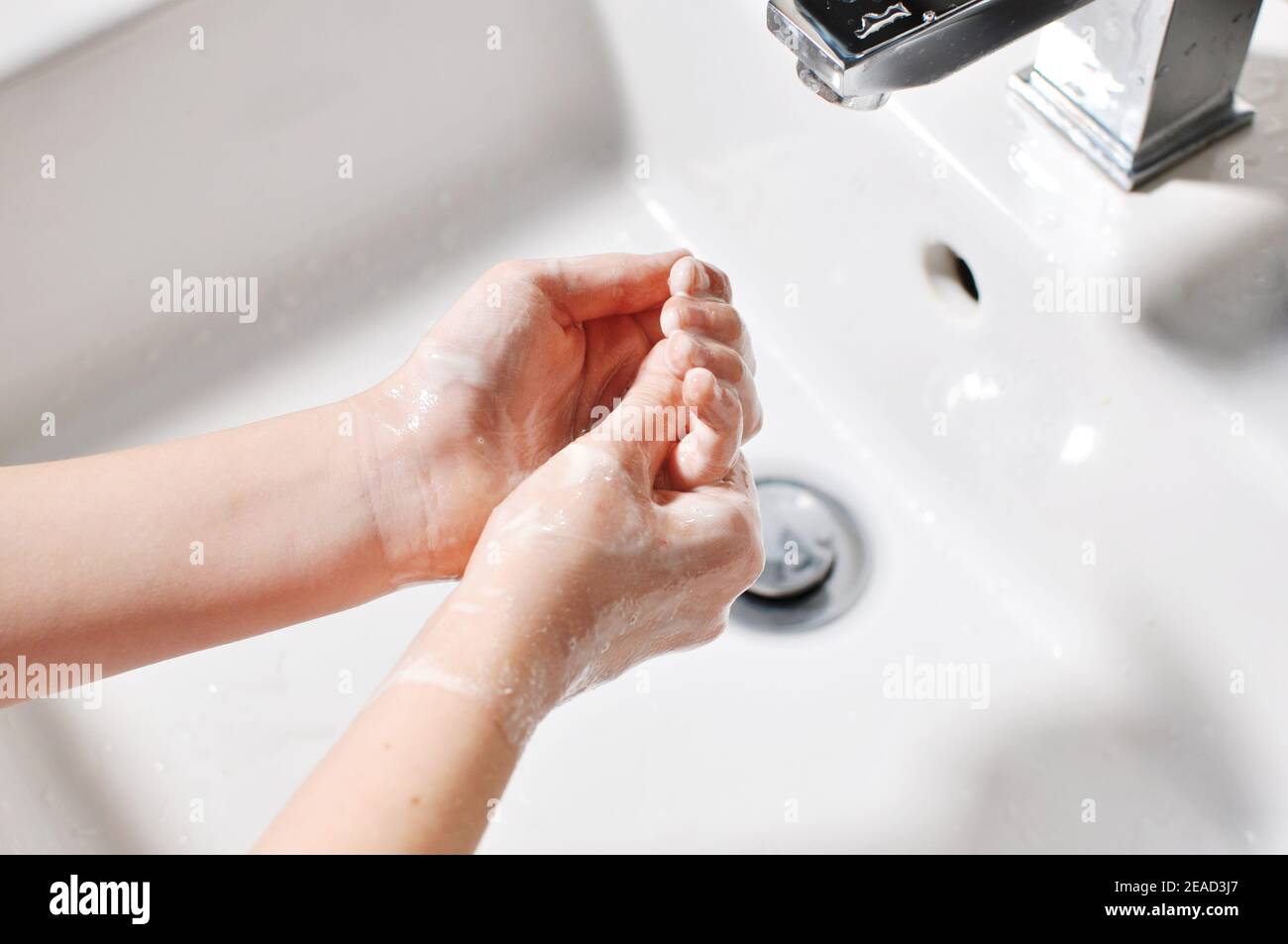 Concept of white European child (girl, kid) cleaning hands with foamy soap over the sink (washbasin). Stock Photo