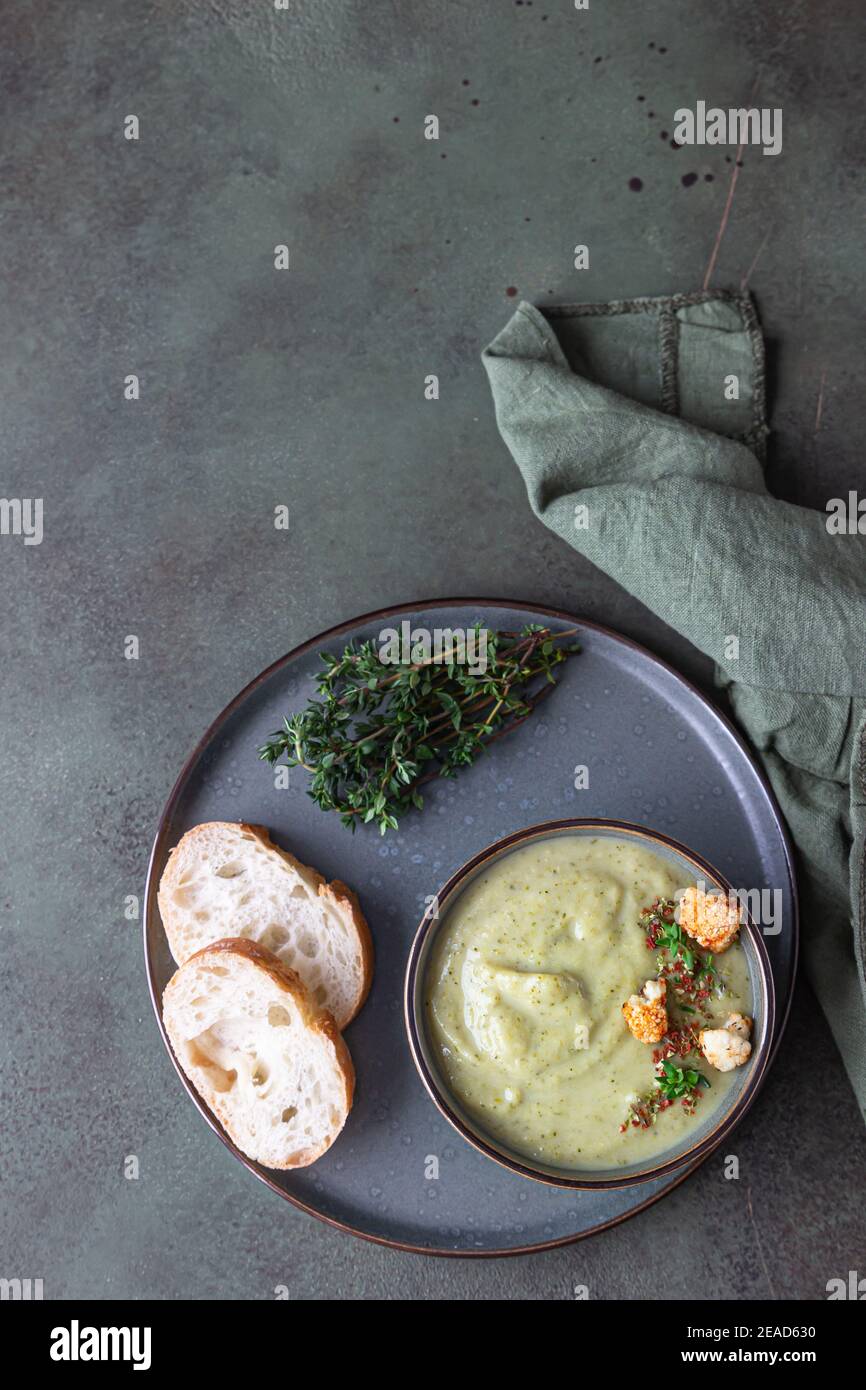 Broccoli cream soup decorated with thyme, cream, roasted cauliflower and fresh bread on green concrete background. Healthy vegetarian food concept. To Stock Photo