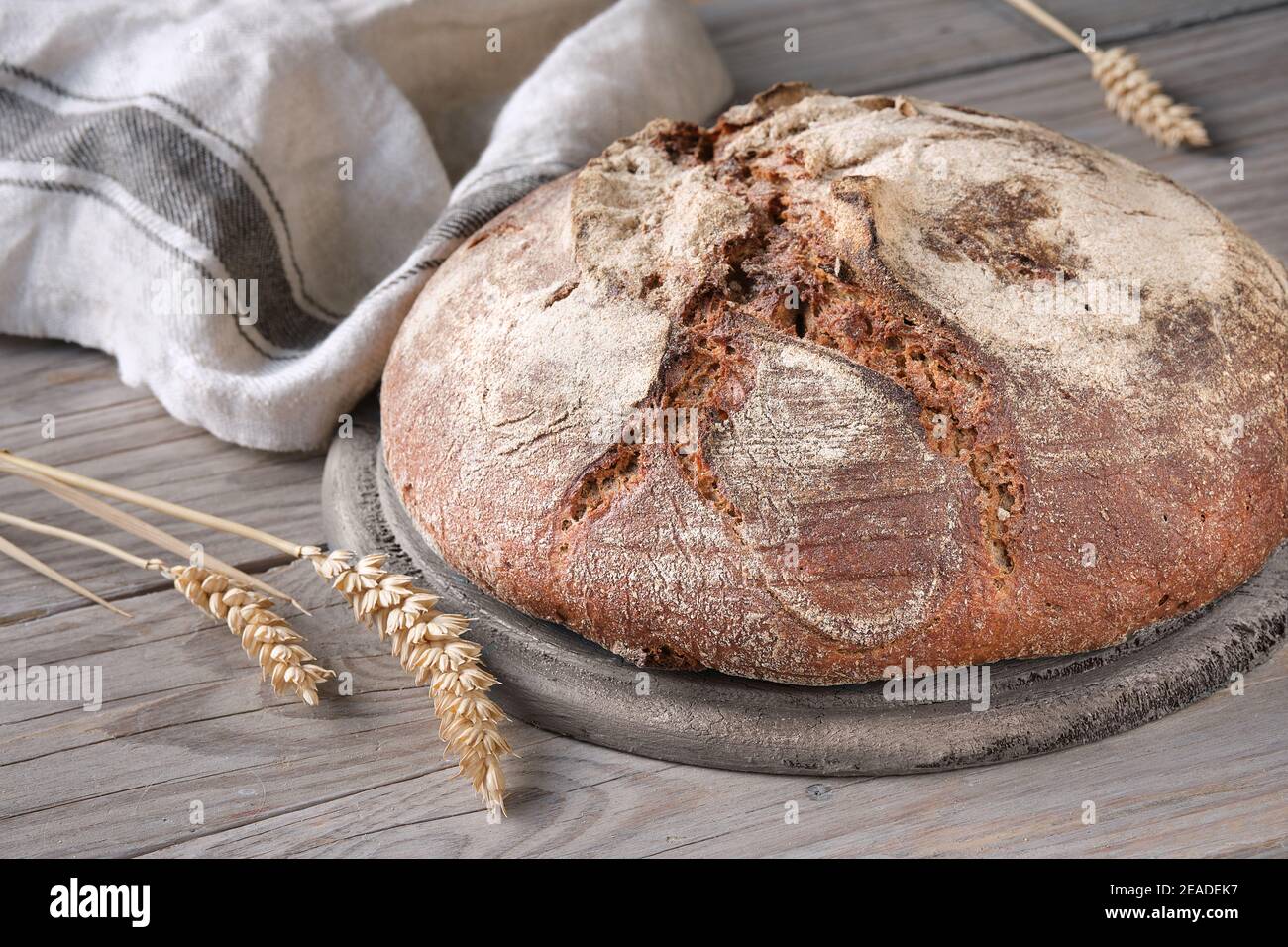 No knead handmade loaf on cutting board on wood with linen towel, spelt ears. German Bauernbrot means Rustic Farmers Bread in English. Wholemeal rye Stock Photo
