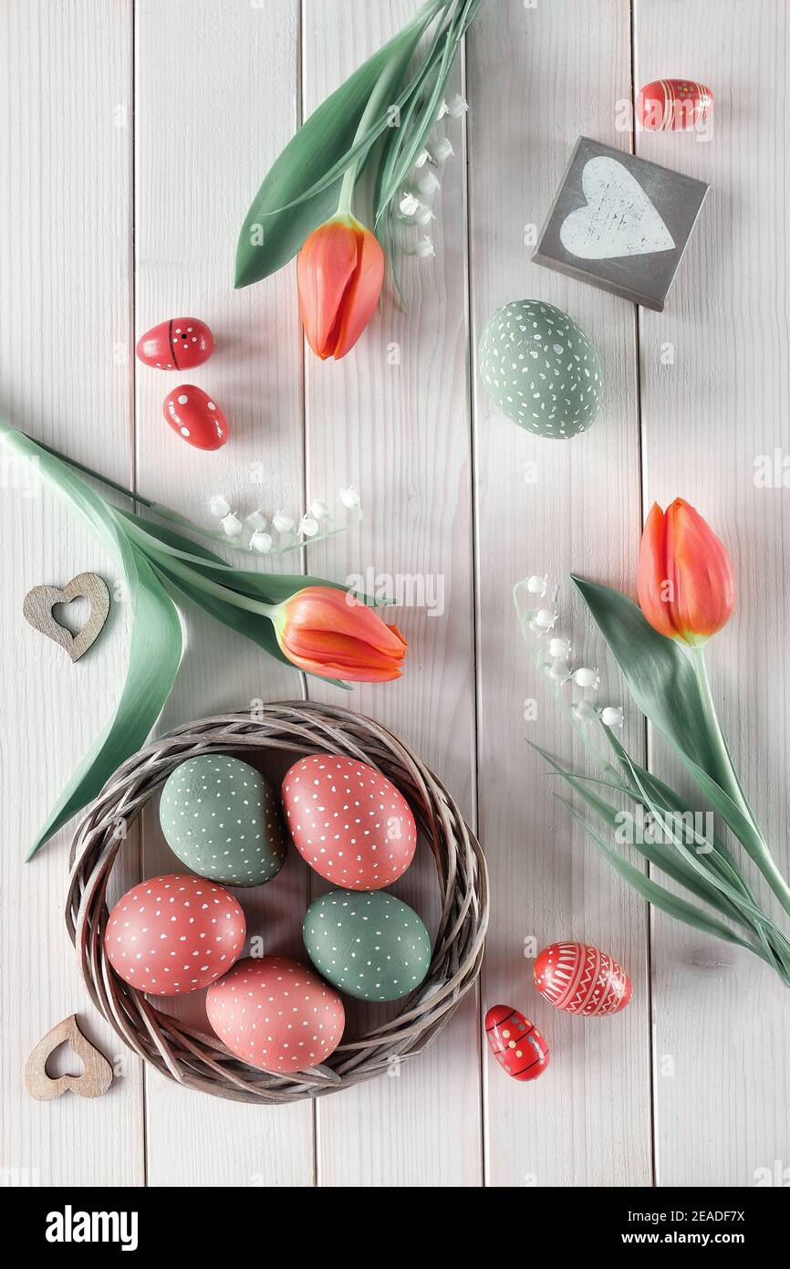 Flat lay with red tulips in rattan wreath basket and green grass. Decorative painted Easter eggs. Spring or Easter background on rustic off white Stock Photo