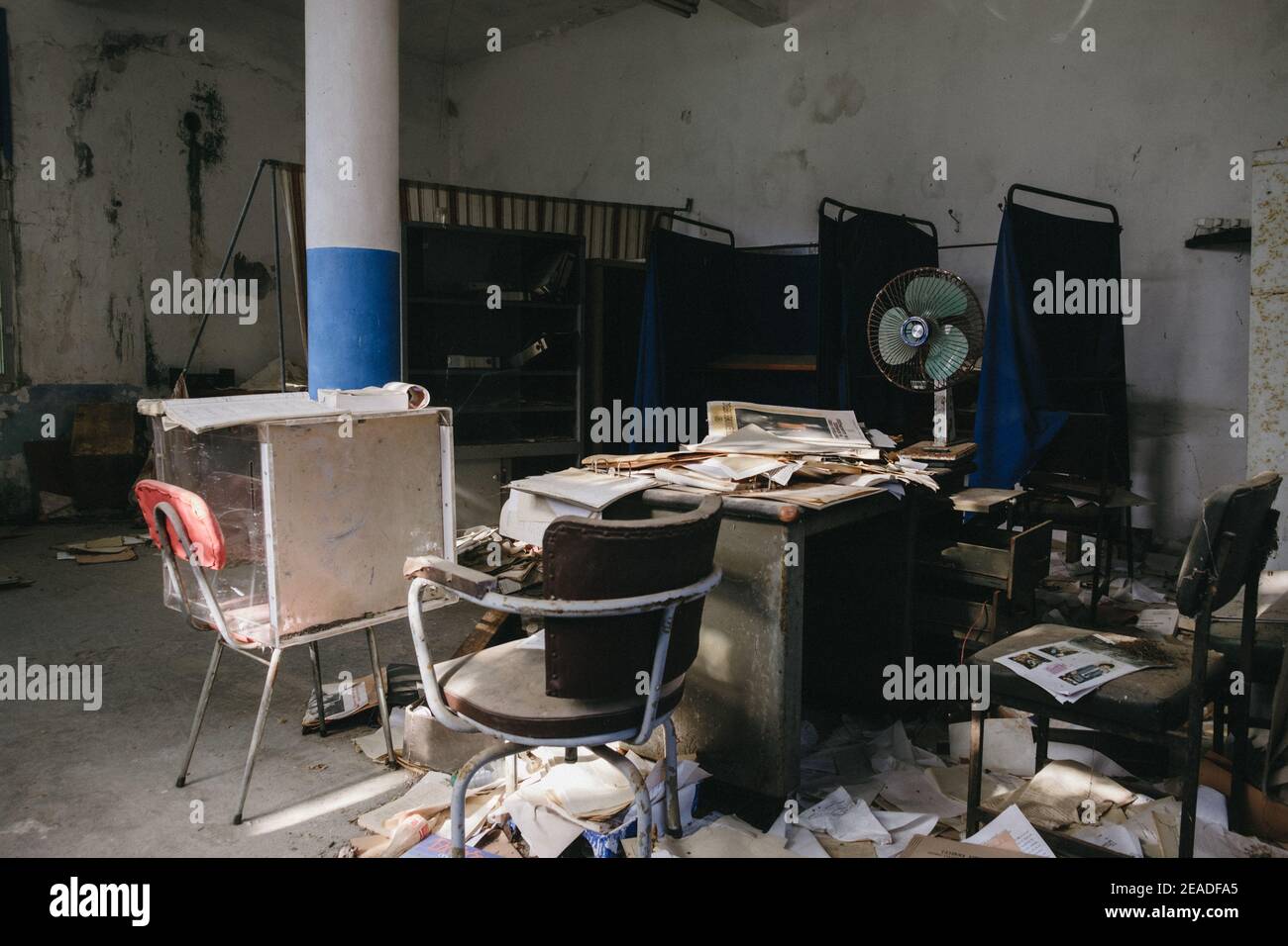 Old abandoned office with tables, chairs, shelves, documents, and a fan Stock Photo