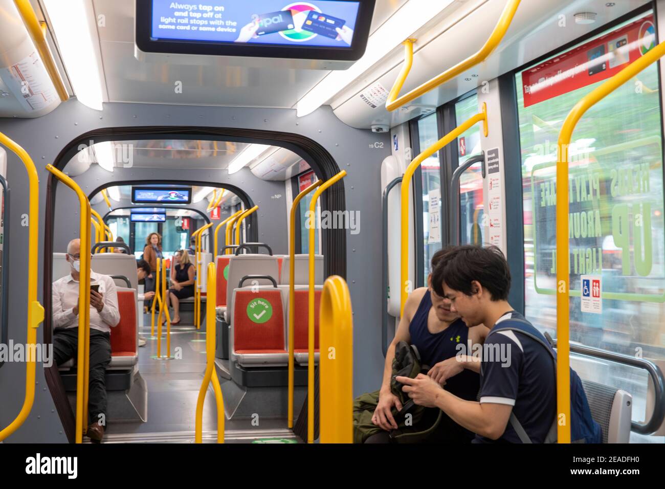 Sydney light rail train carriage interior, passengers commuting, sit here stickers act as social distancing during covid 19 pandemic,Sydney,Australia Stock Photo