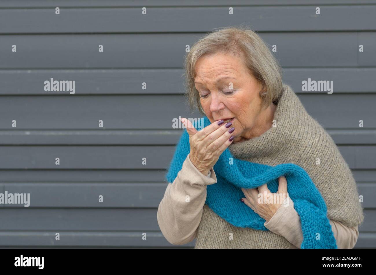 Elegant senior woman coughing into her hand while clutching her chest