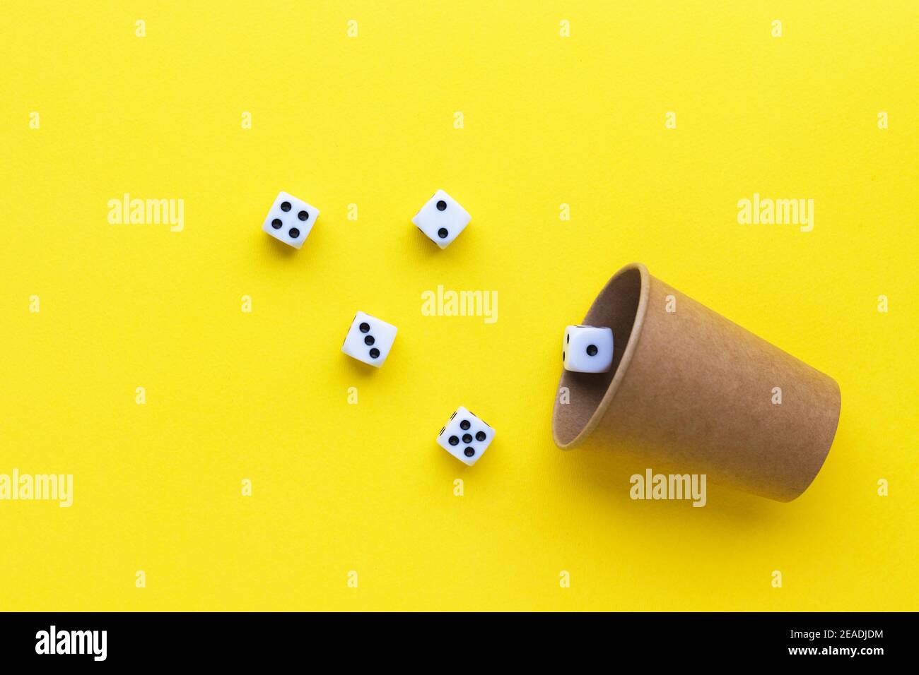 Gaming dice and cardboard cup on yellow background. Playing cube with numbers. Items for board games. Flat lay, top view with copy space. Stock Photo
