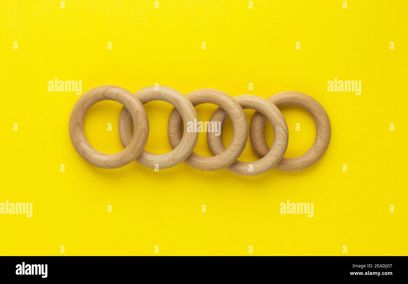 Five wooden rings on yellow background. Natural wood baby teether. Eco-friendly children toy. Top view, flat lay with copy space. Stock Photo