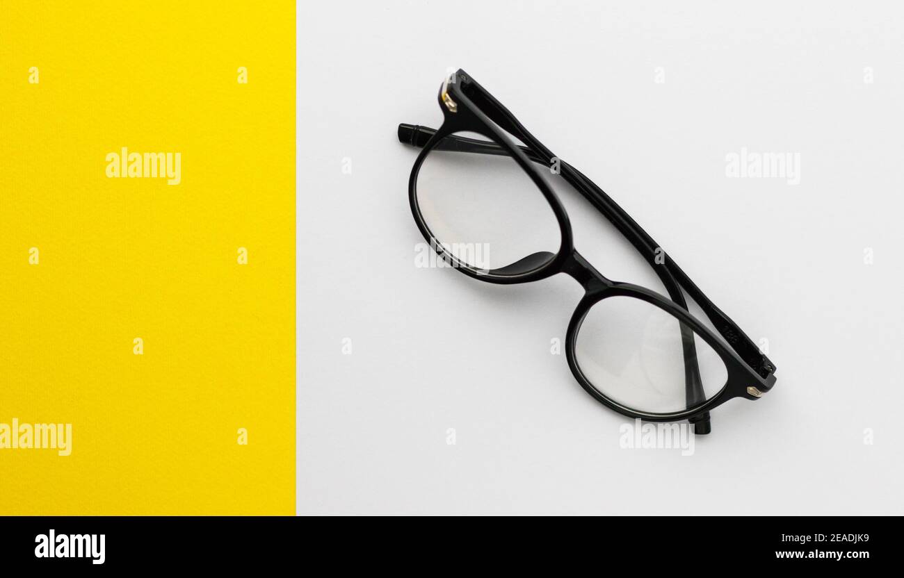 Eyeglasses with black frame on white-yellow background. Eye glasses. Round glasses with transparent lenses. Close up eyeglasses with blurry technique. Stock Photo