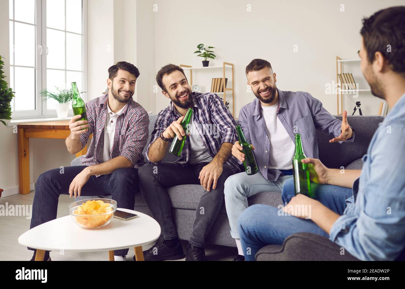 Group of happy friends sitting on sofa, drinking beer, sharing funny stories and laughing Stock Photo