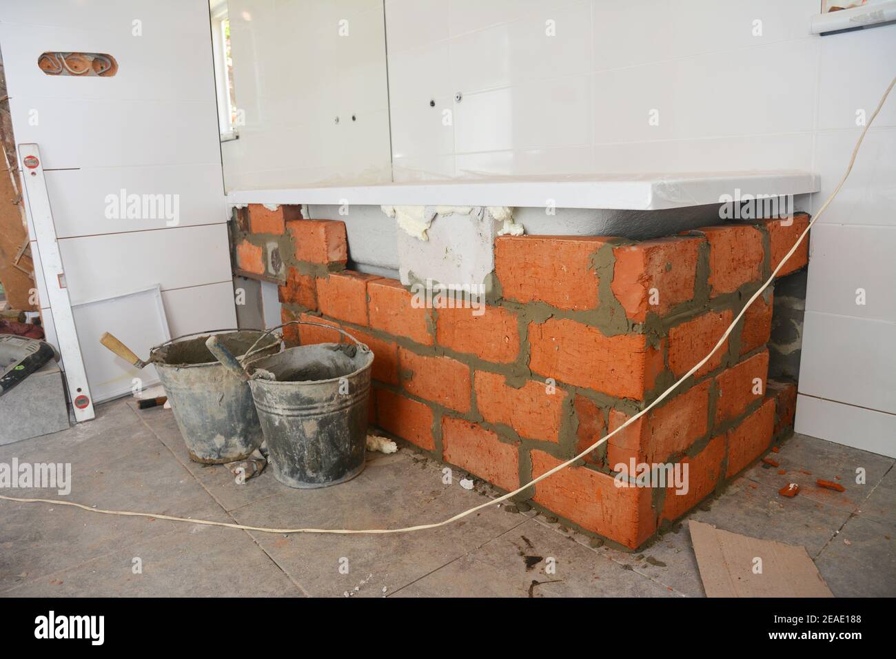New acrylic bathtub installation near the mirror and laying bricks around a tub to tile it later while bathroom remodel, bath renovation. Stock Photo