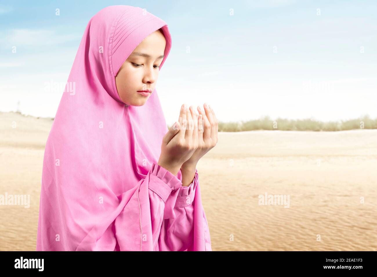 Asian Muslim woman in a veil standing while raised hands and praying ...