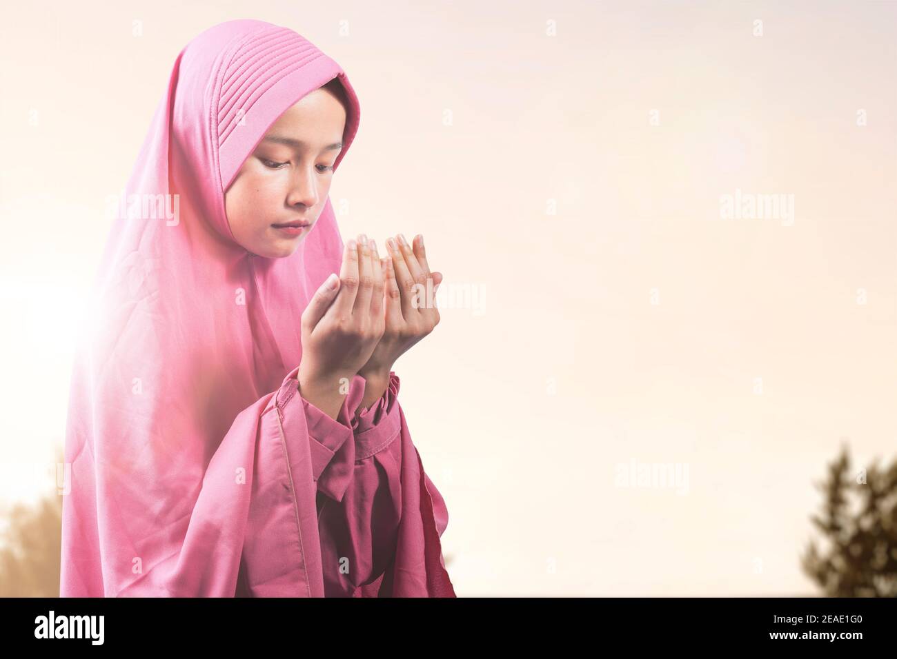 Asian Muslim woman in a veil standing while raised hands and praying ...
