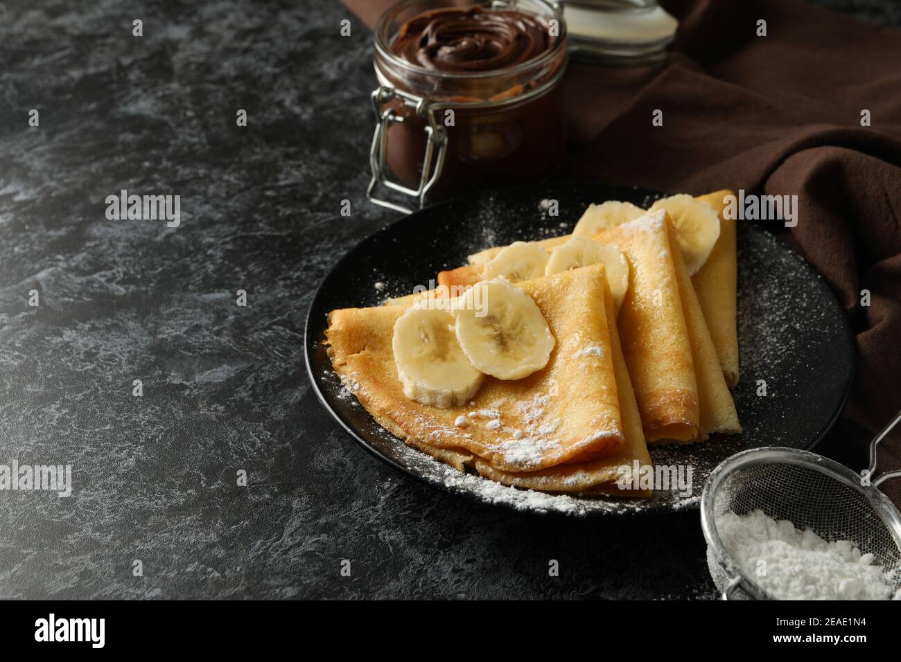 Concept of delicious breakfast with crepes with sugar powder and banana on black smokey background Stock Photo