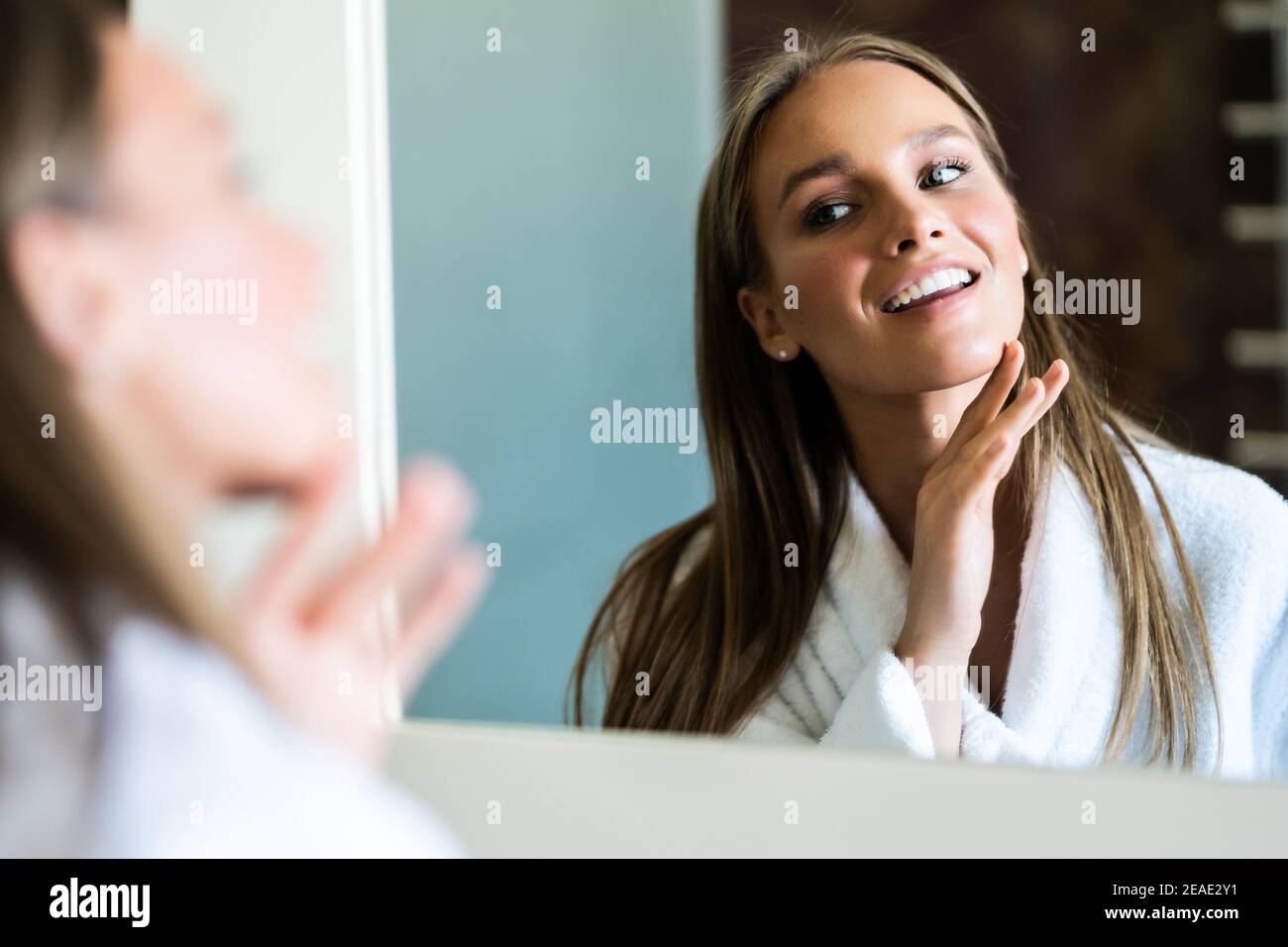 Beautiful woman is touching her face and smiling while looking at the ...