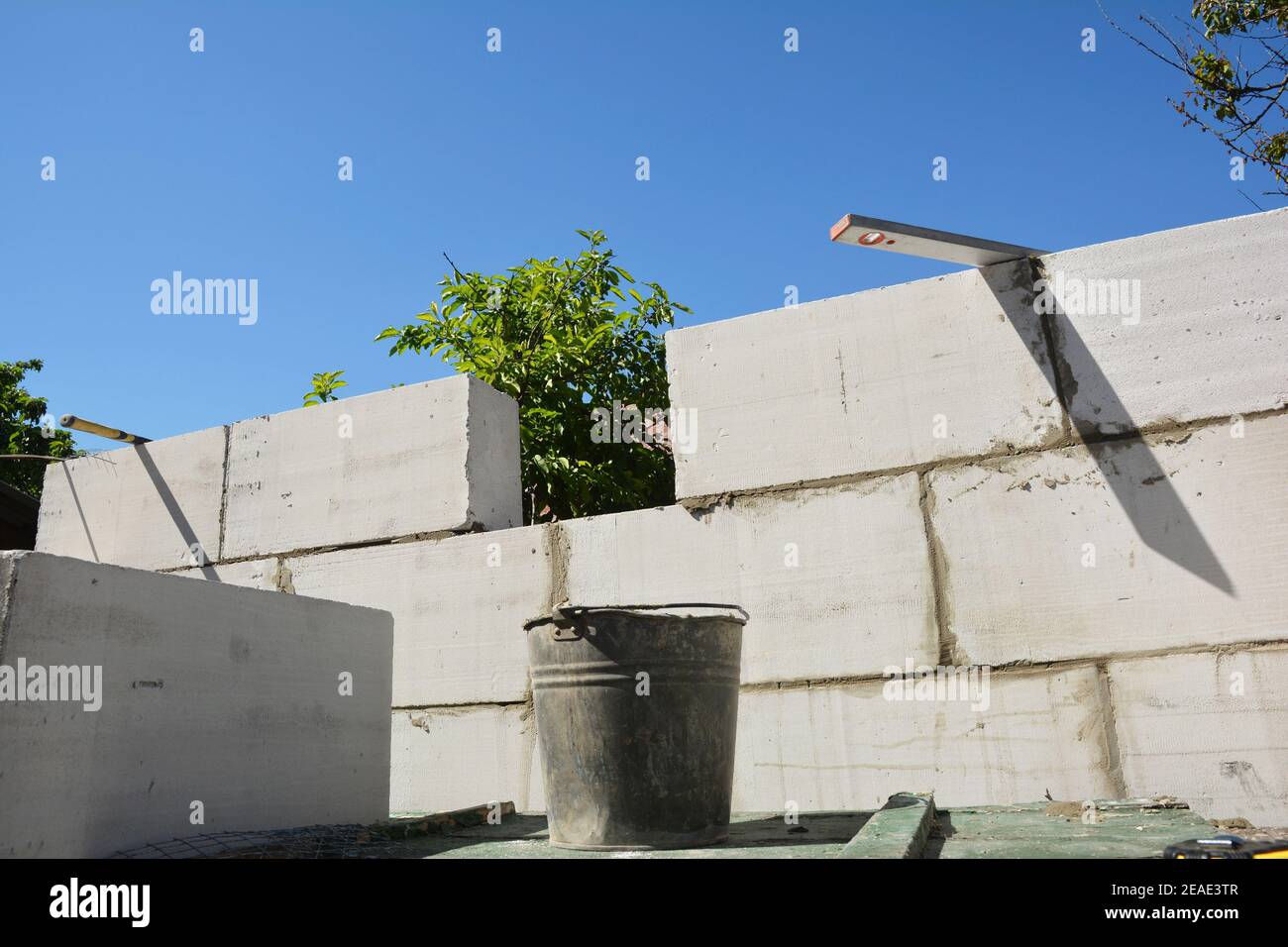 A close-up on home addition, house wall construction from autoclaved aerated concrete blocks using a trowel, mortar in a bucket and spirit level. Stock Photo