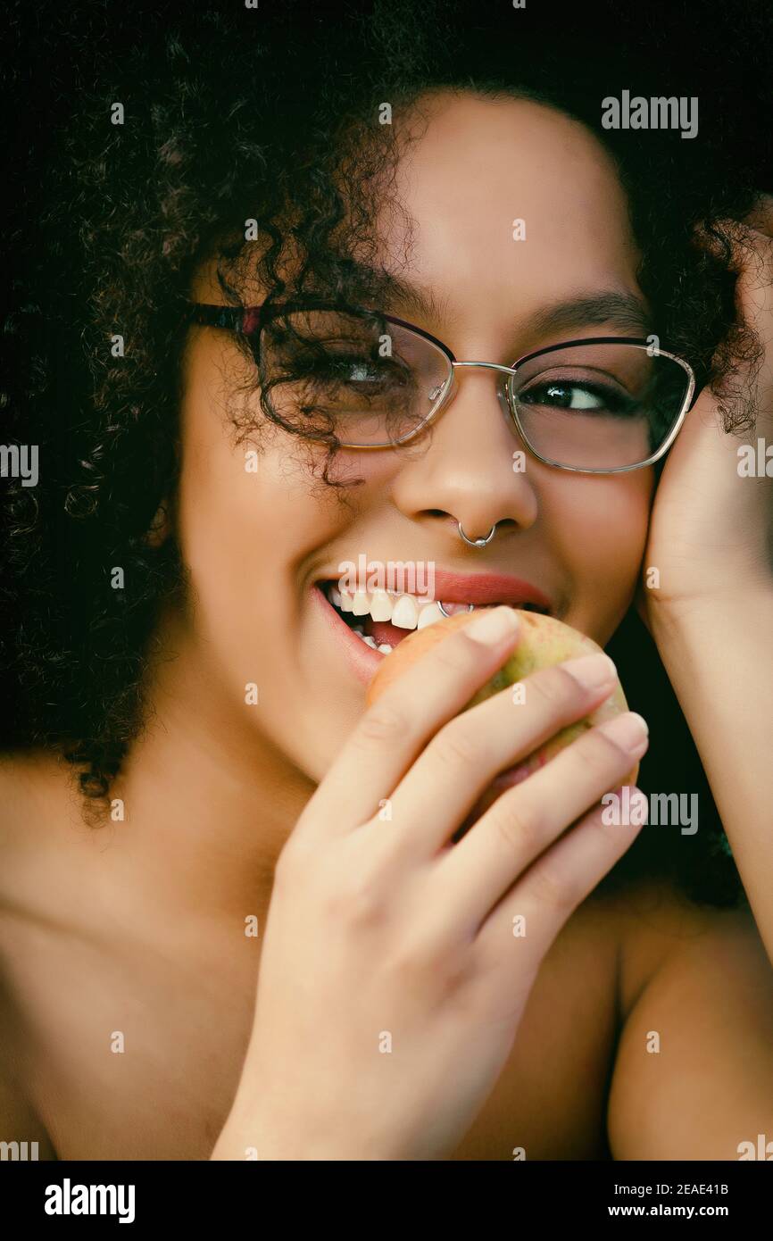Stunning black Female model for editorial photo shoot, wearing glasses and smiling, eating an apple in natural light Stock Photo