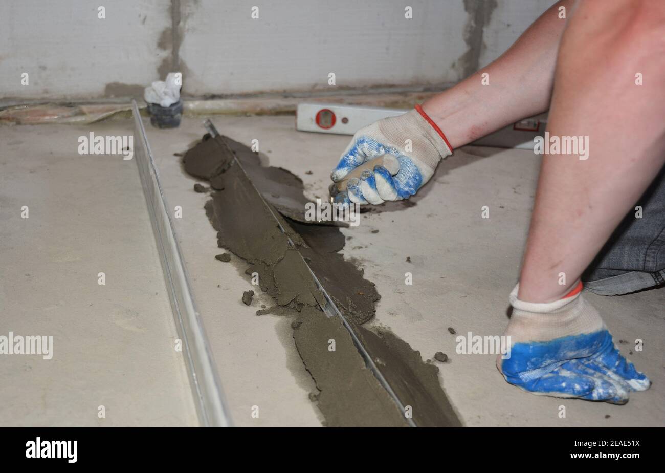 A building contractor is leveling concrete floor using steel beams and plastering after removing them using a spade trowel. Stock Photo