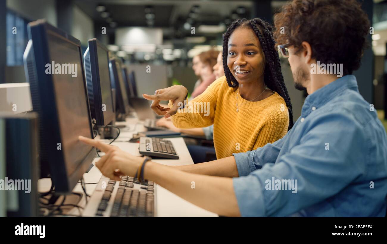 University Library: Bright Black Girl and Smart Hispanic Boy Together Work on Computers, Chat, Discuss Class Assignment, Explain and Advice Each Other Stock Photo