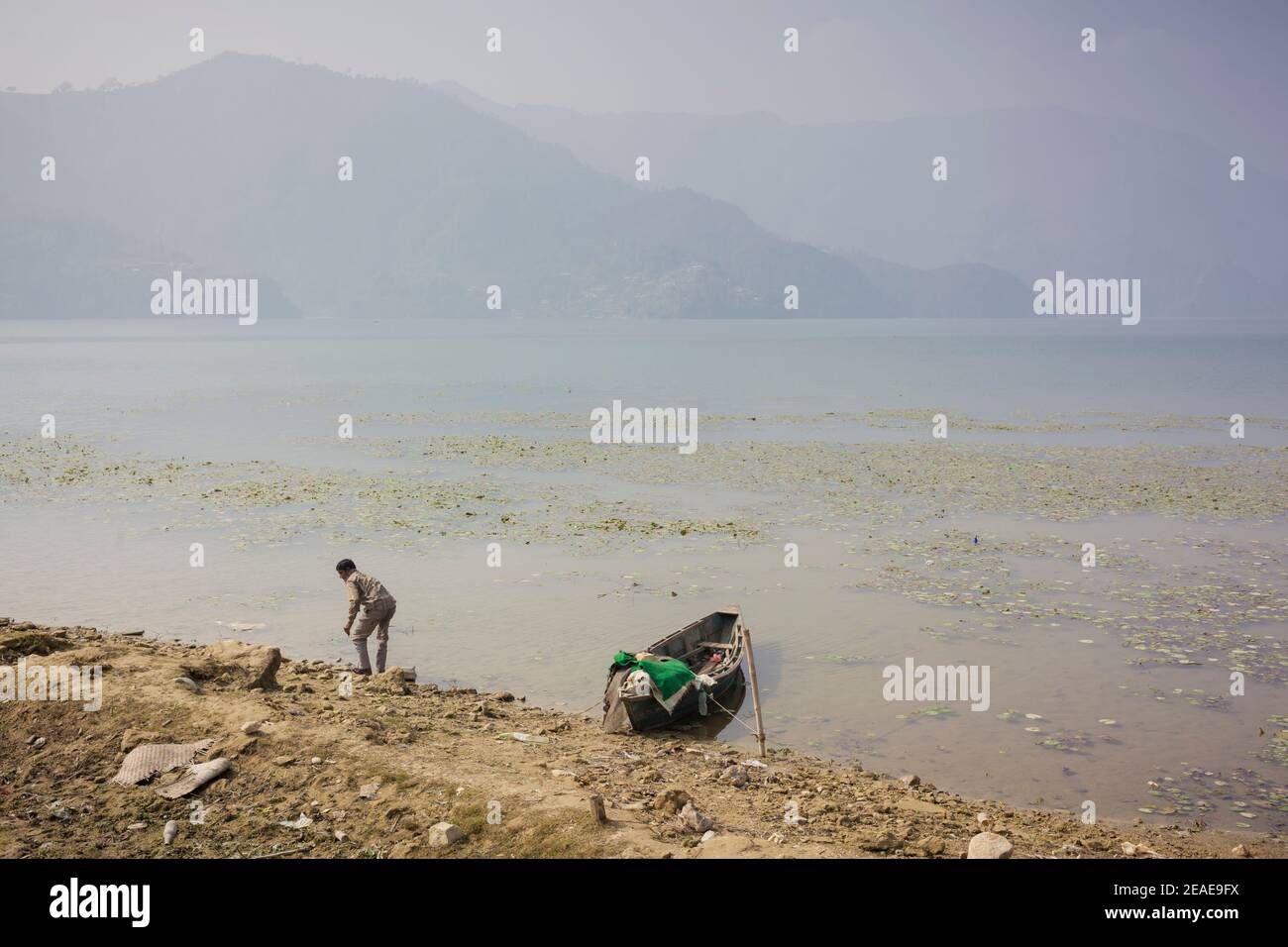 A local man with his wooded boat on the shore of Pewa Lake. Pokhara. Nepal. Stock Photo