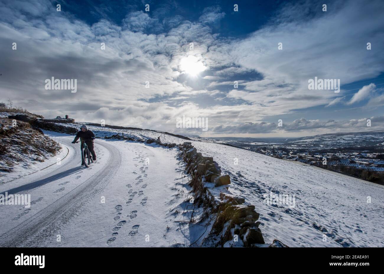 Haslingden, East Lancashire, England, 9th February 2021. A fresh blanket of snow covers the town of Haslingden as the freezing weather continues in the North West of England this week. A cyclist rides down the snow covered roads above the town. Credit: Paul Heyes/ Alamy Live News Stock Photo