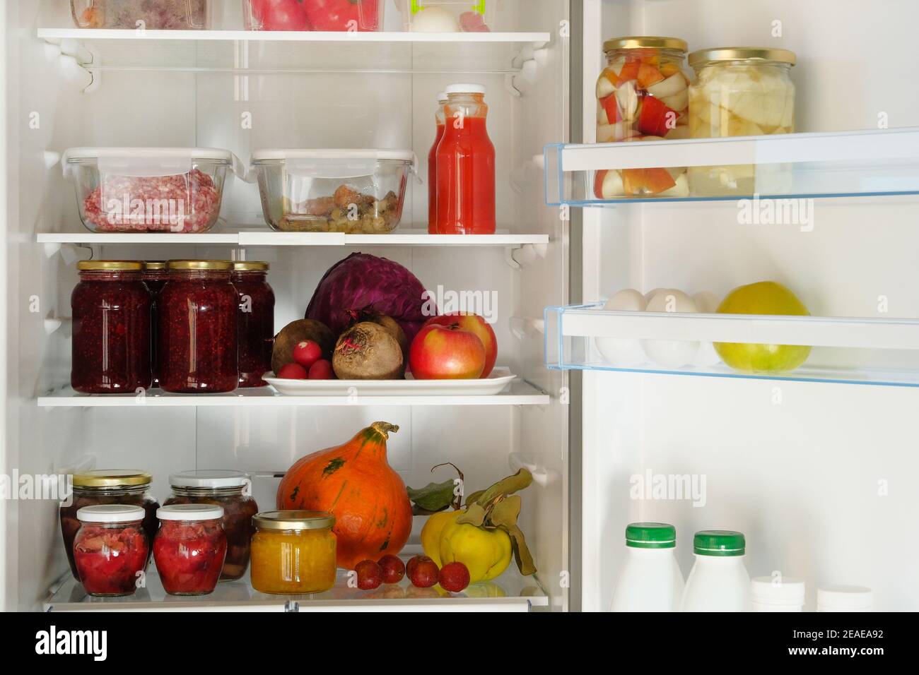 Jars with homemade fruit and berry jams, juices and other products on shelf in fridge. Fermented healthy foods stand in refrigerator. Stock Photo