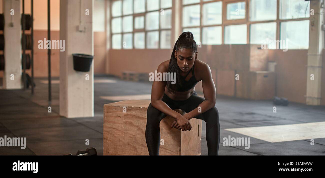 Exhausted looking young Indian woman in sportswear taking a break for a workout session in a gym Stock Photo