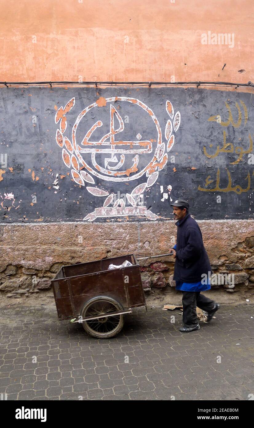 Marrakesh. Man with wheelbarrow near Jemaa el Fna Square, Marrakesh, Morocco. Painted wall with Arabic calligraphy in the background. Stock Photo