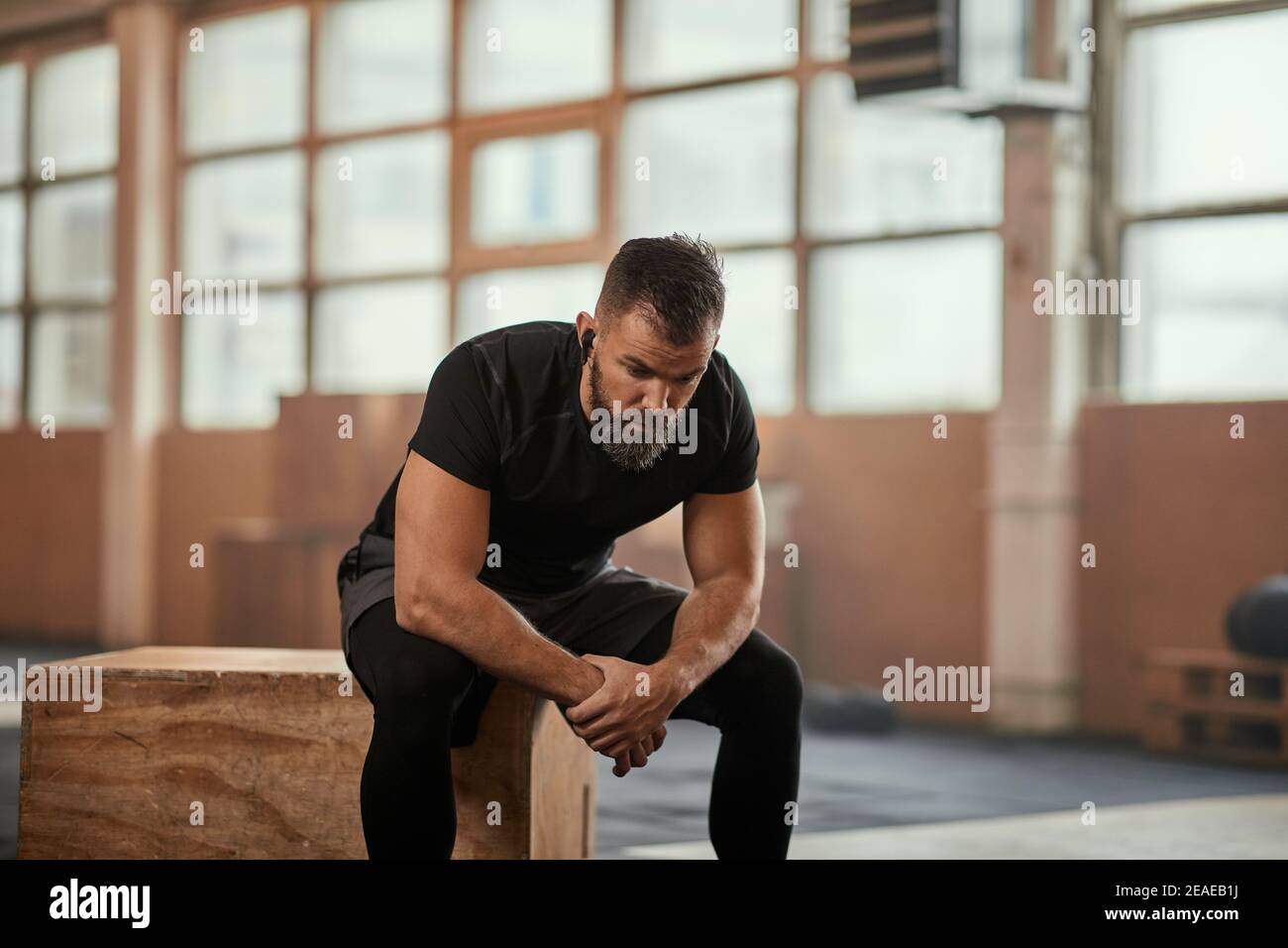 Fit young man in sportswear sitting on a box in a gym and looking exhausted after a workout session Stock Photo