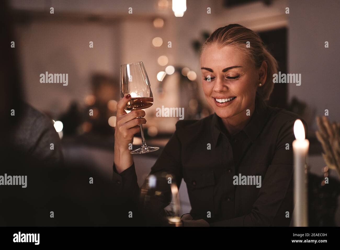 Smiling young woman sitting at a dining room table during a candlelit dinner party drinking wine Stock Photo