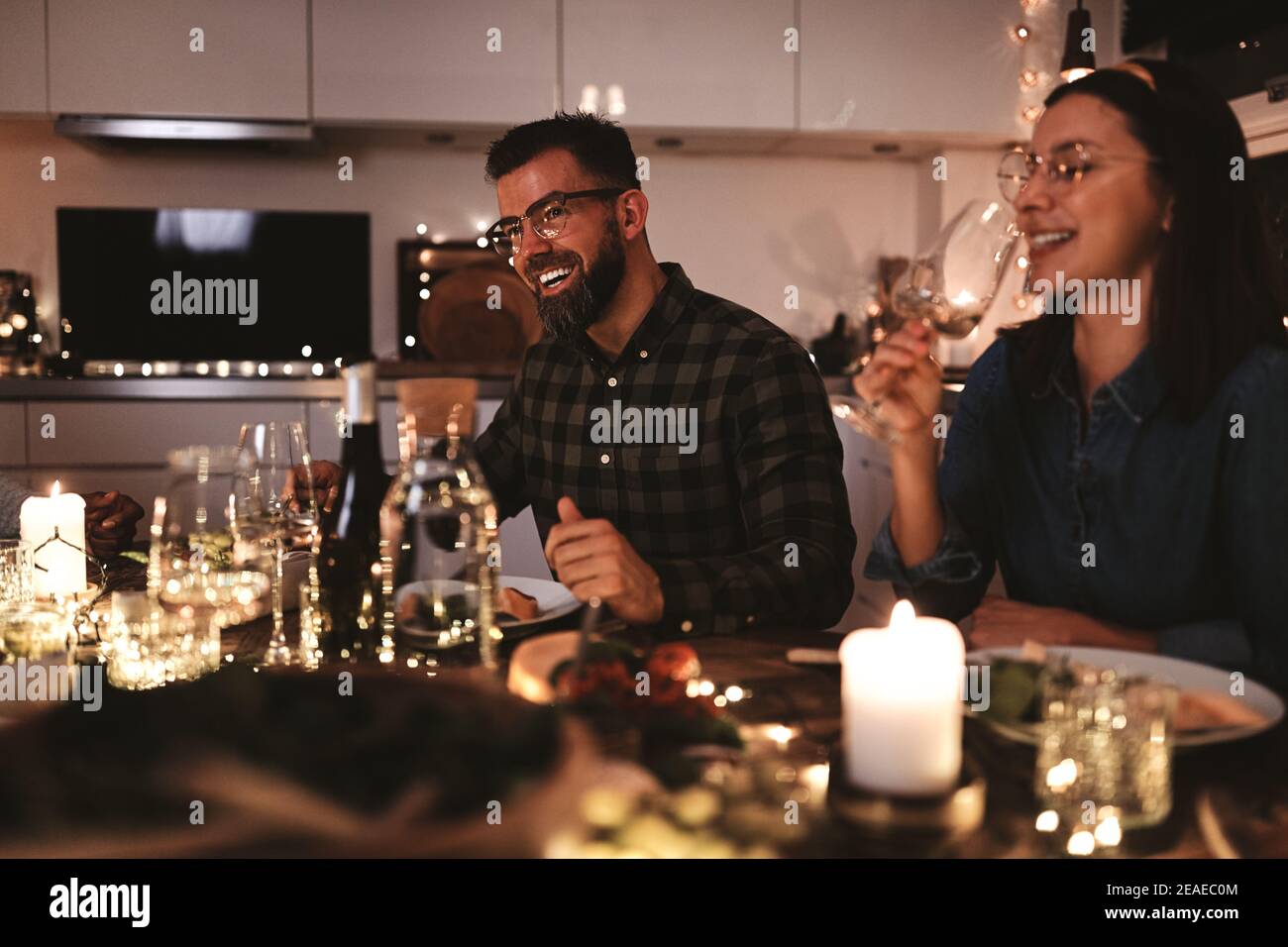Friends laughing together over glasses of wine while sitting around a table during a candlelit dinner Stock Photo