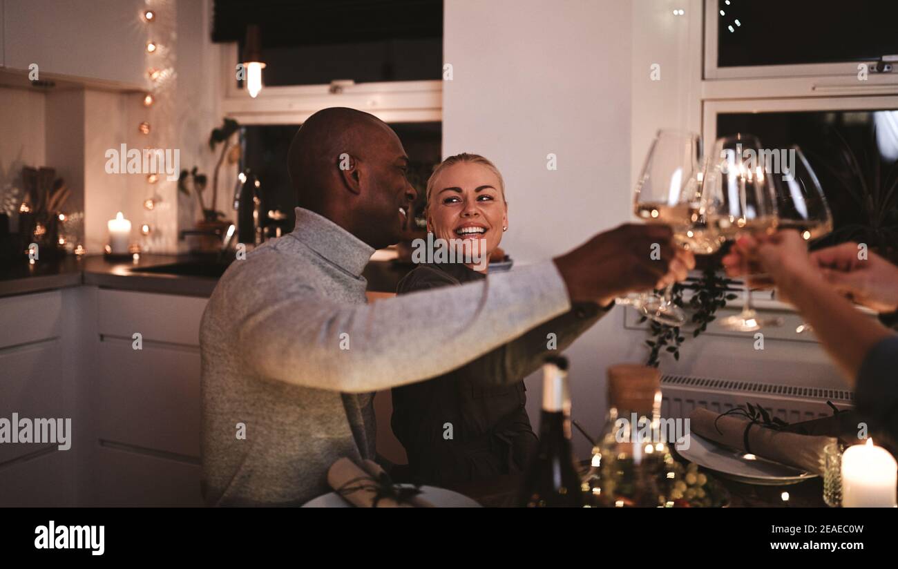 Laughing couple toasting friends with wine while sitting together at at table during a candlelit dinner party Stock Photo