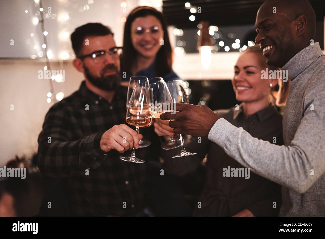 Diverse group of smiling friends toasting together with drinks in a kitchen before an evening dinner party Stock Photo