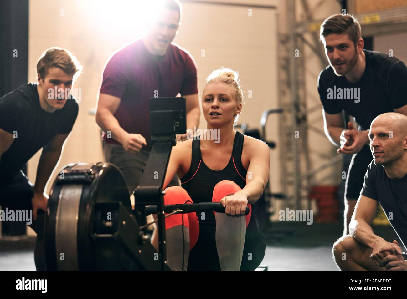 Fit young woman being supported by a group of gym friends during a workout on a rowing machine Stock Photo