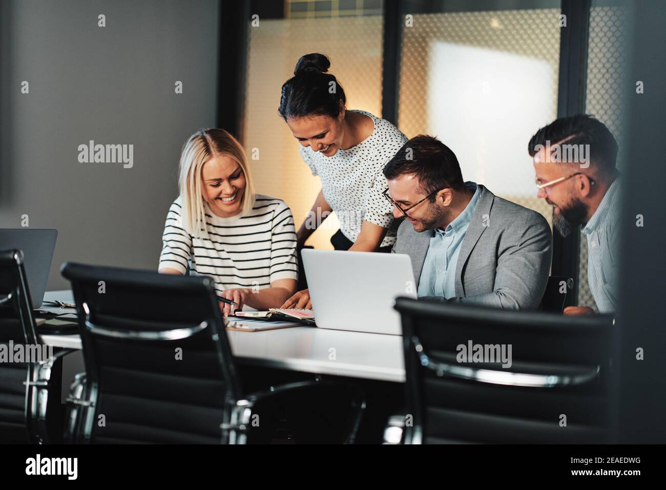 Laughing group of businesspeople working together on a laptop and discussing paperwork at a table during a boardroom meeting Stock Photo