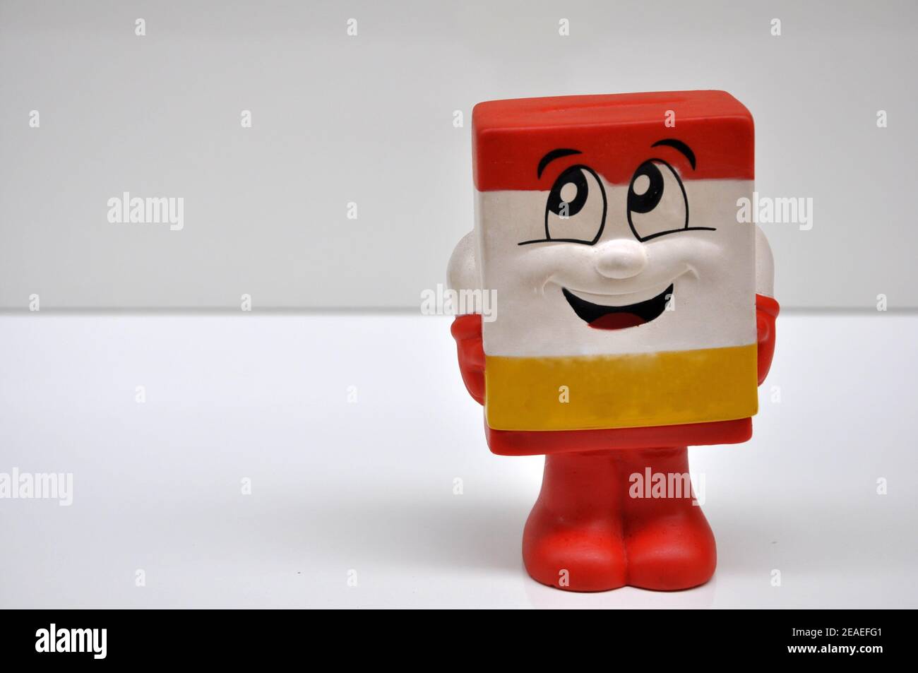 Mascot style vinyl doll with a smiley face for children with the motive of saving coins and money in yellow, white and red on white background Stock Photo