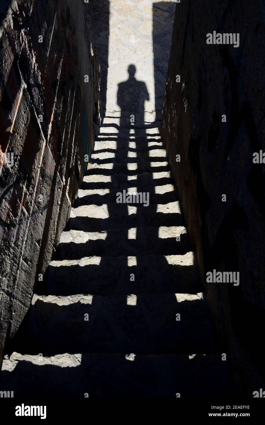 Mysterious Image of Long Shadow of Man on Stairs, Steps or Staircase in Dark, Dingy Alley or Alleyway Stock Photo