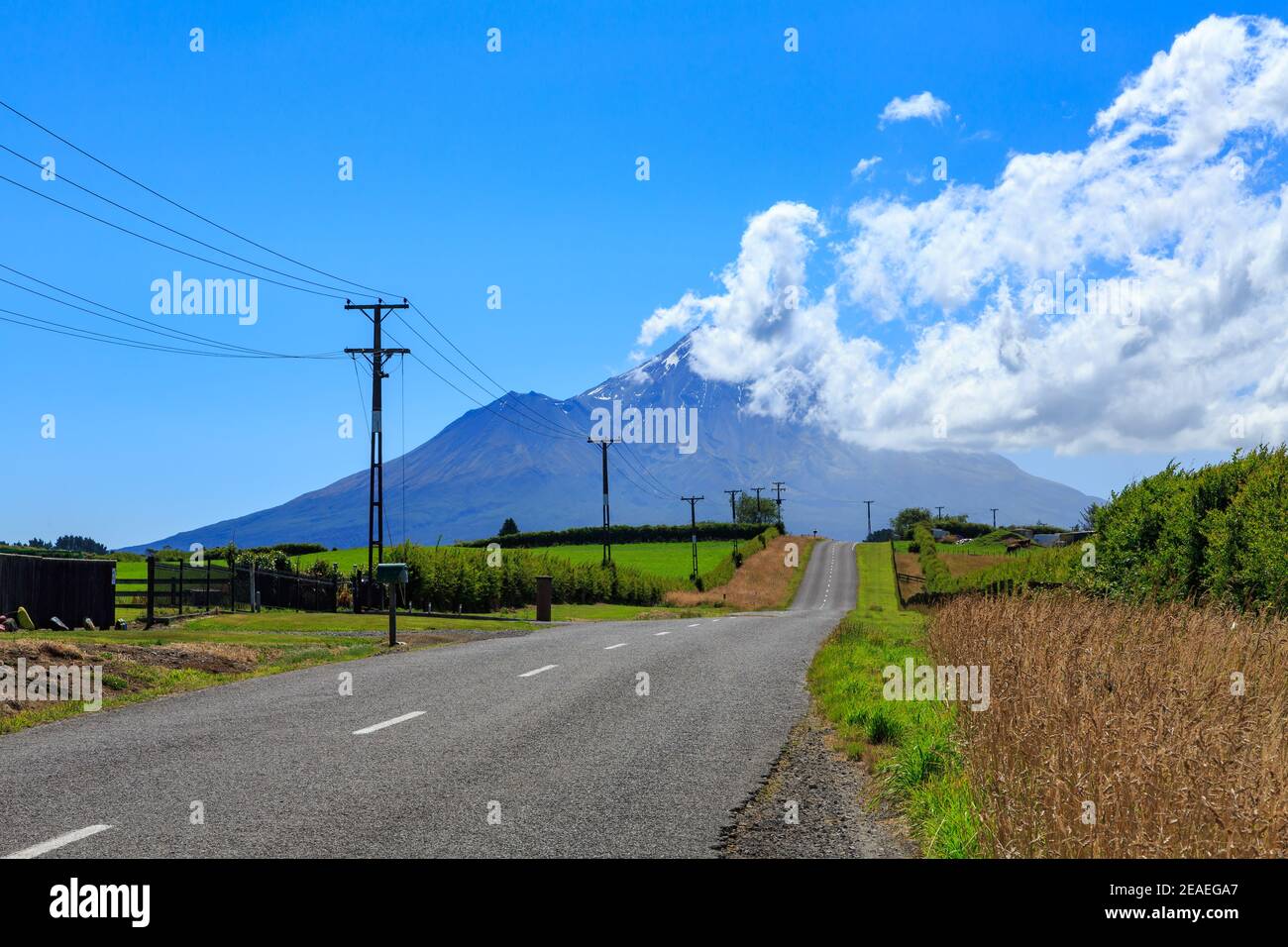 A road leading to Mount Taranaki, New Zealand. Summer clouds swirl around the mountain's peak Stock Photo