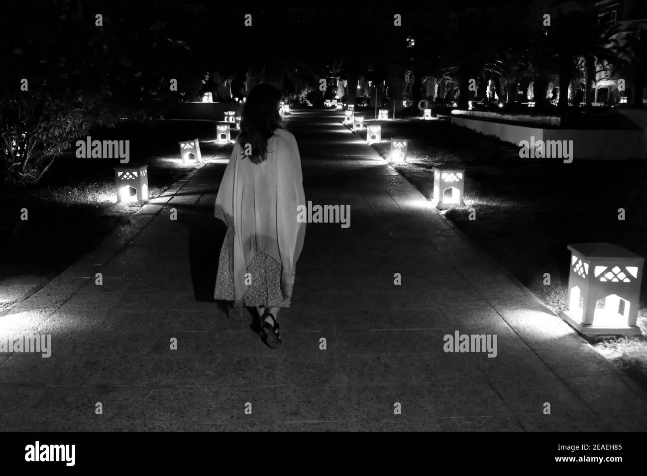 woman goes at night on path among of lights lantern, monochrome Stock Photo