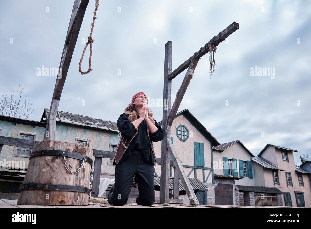 A young woman in black clothes is praying next to the gallows on her knees Stock Photo