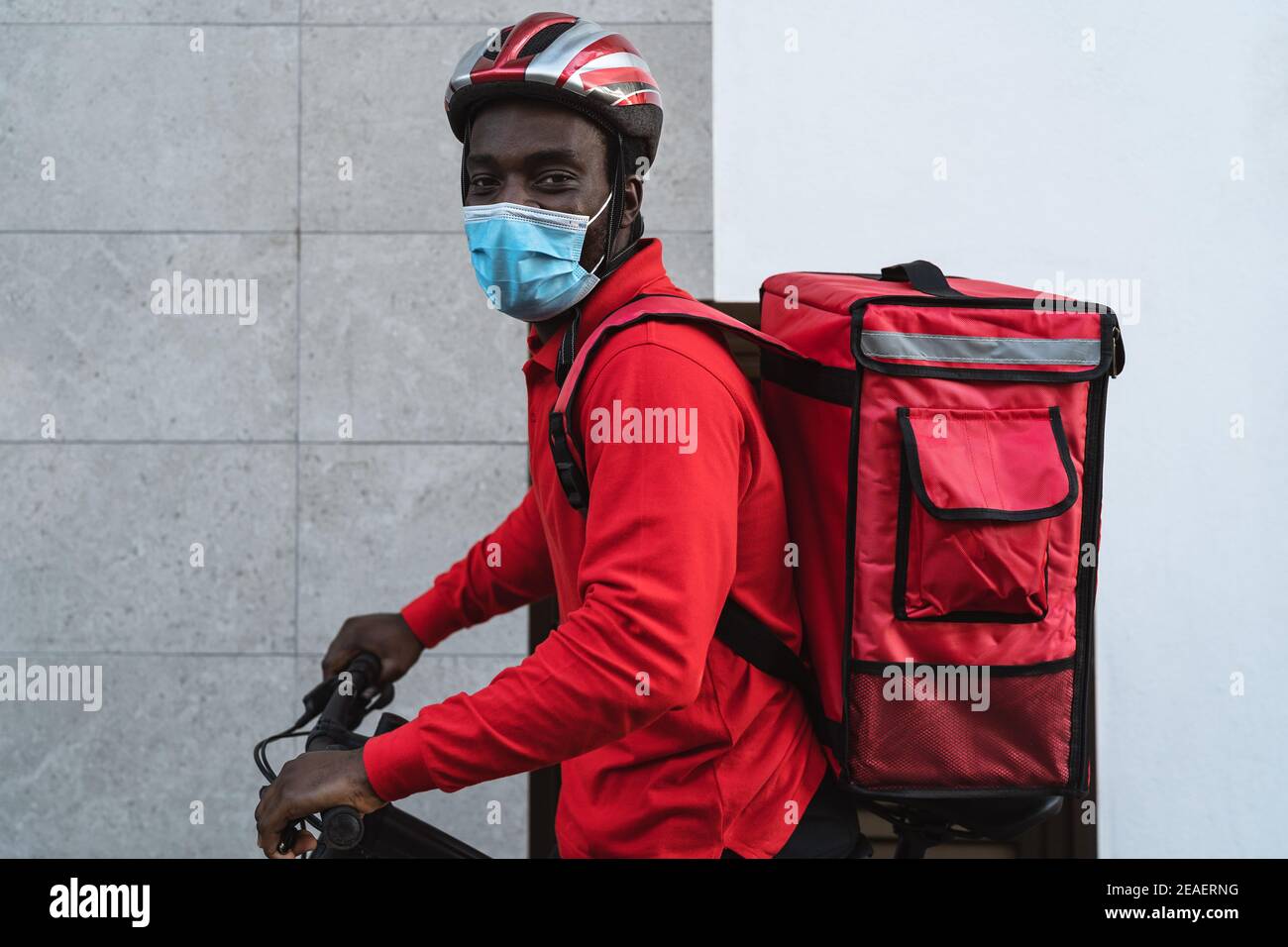 African rider man delivering meal to customers with electric bicycle while wearing face mask during corona virus outbreak Stock Photo