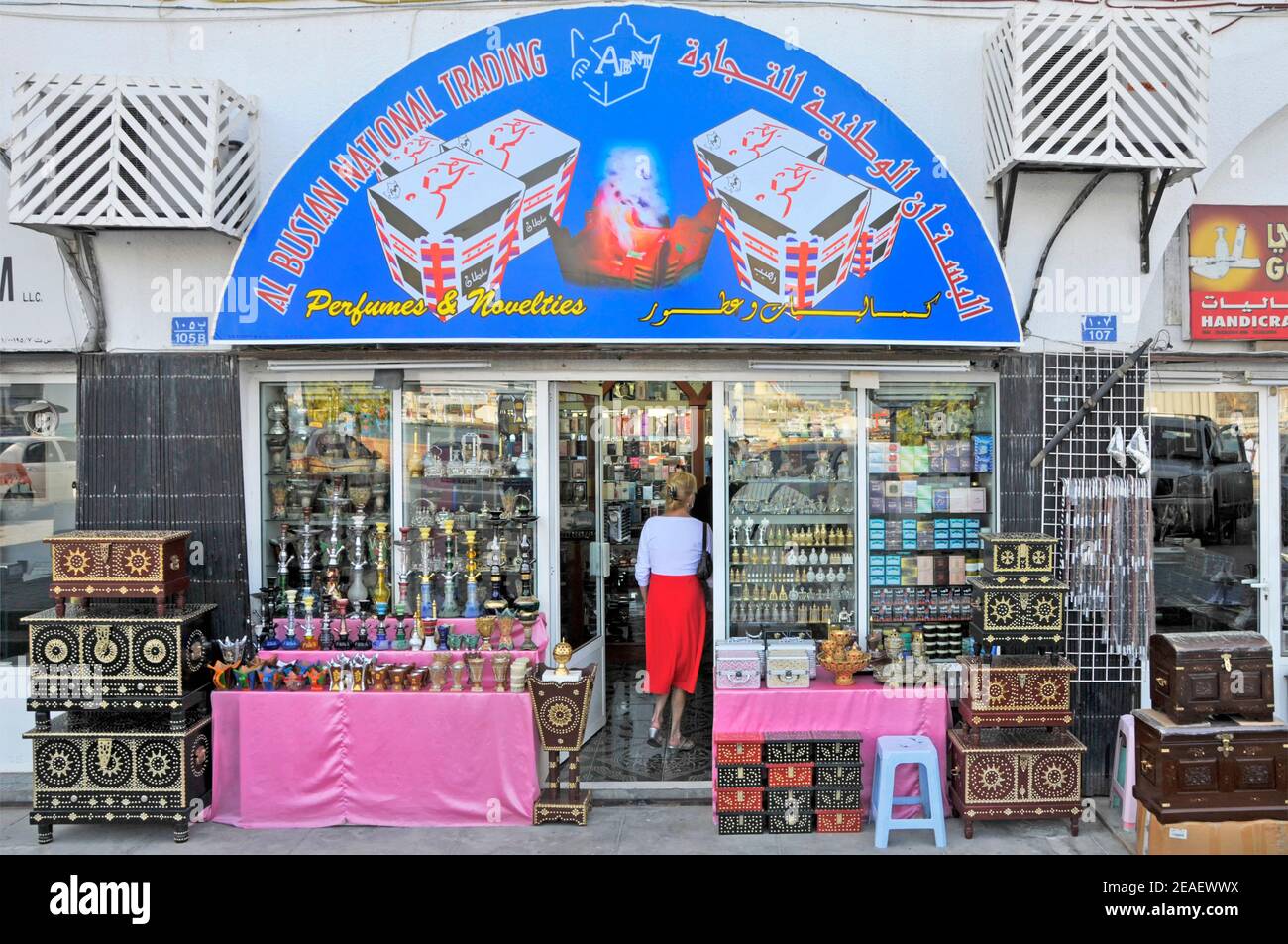 Store window & merchandise back view of woman entering a shop front selling perfumes & novelties on corniche road in Mutrah Muscat  Oman Middle East Stock Photo