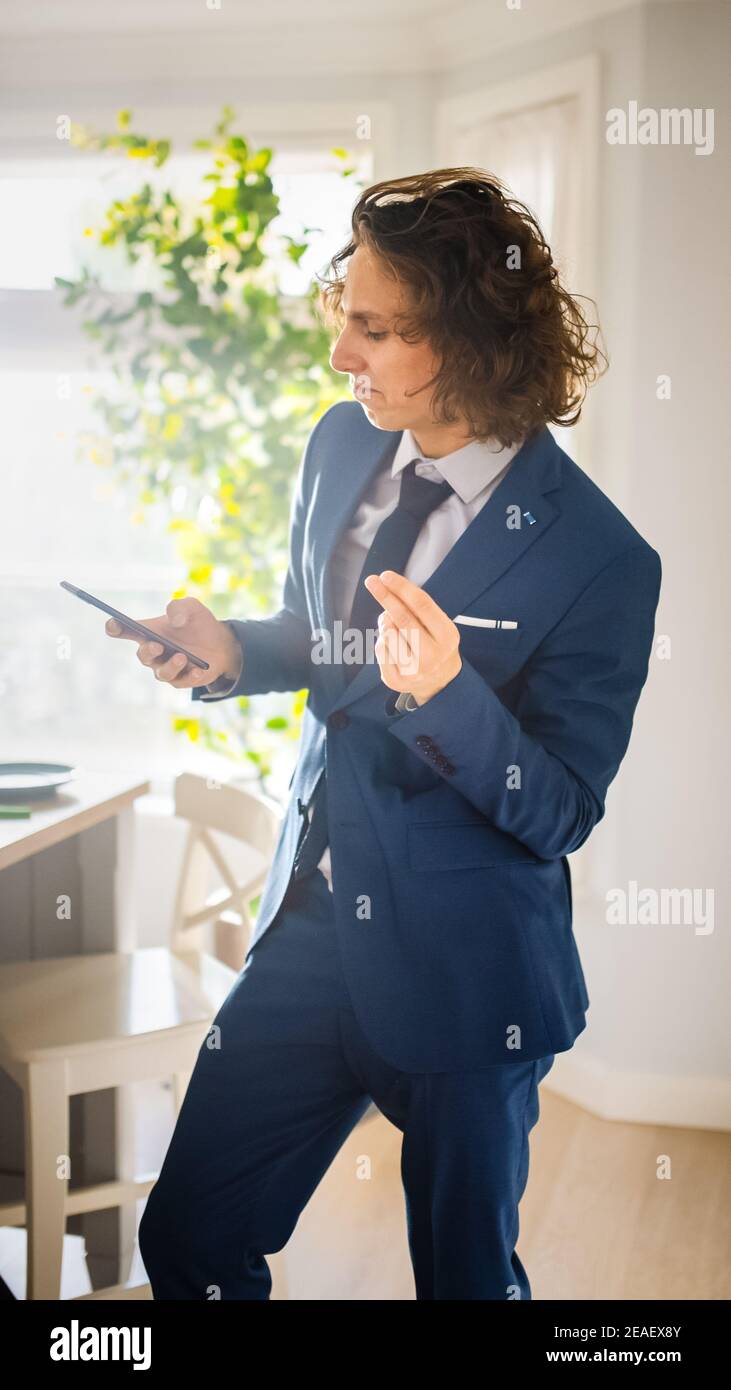 Happy Young Man with Long Hair Dancing at Home while Wearing Blue Business  Suit. He is Listening to Music on a Mobile. Energetic Man Using Smartphone  Stock Photo - Alamy