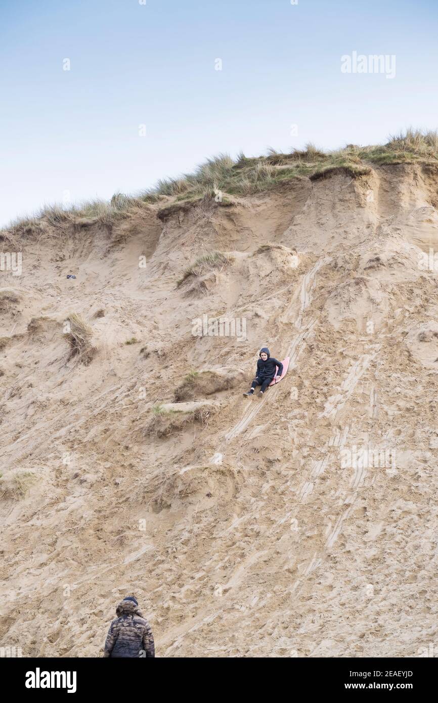 A young boy sliding down and damaging a sand dune at Crantock Beach in Newquay in Cornwall. Stock Photo