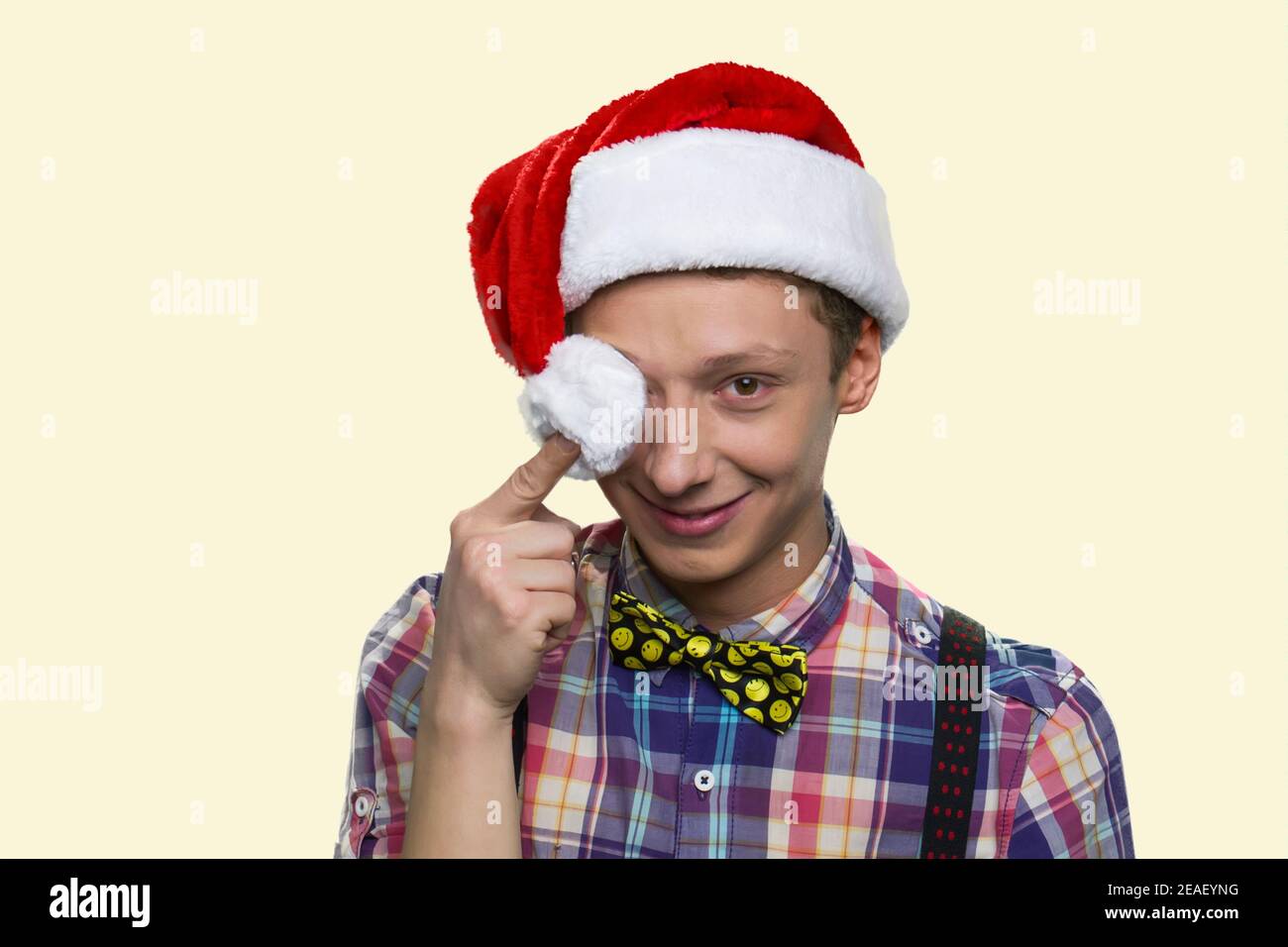 Smiling teen boy is closing his eye with santa hat's pompon. Stock Photo