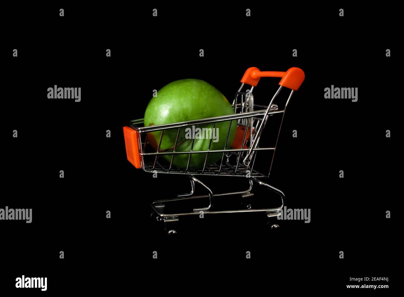 Fresh organic green apples in a mini shopping trolley. Healthy fruits. Black background. Stock Photo