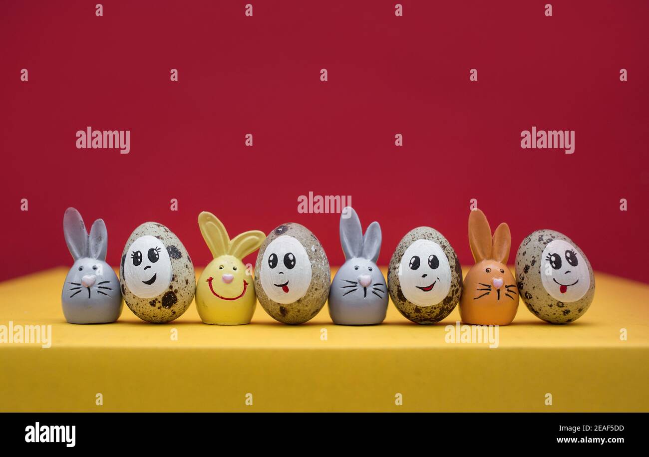 colorful cute Easter bunnies, Easter quail eggs with painted smiles and eyes stand next to each other in a row. Funny decorations for the spring holid Stock Photo