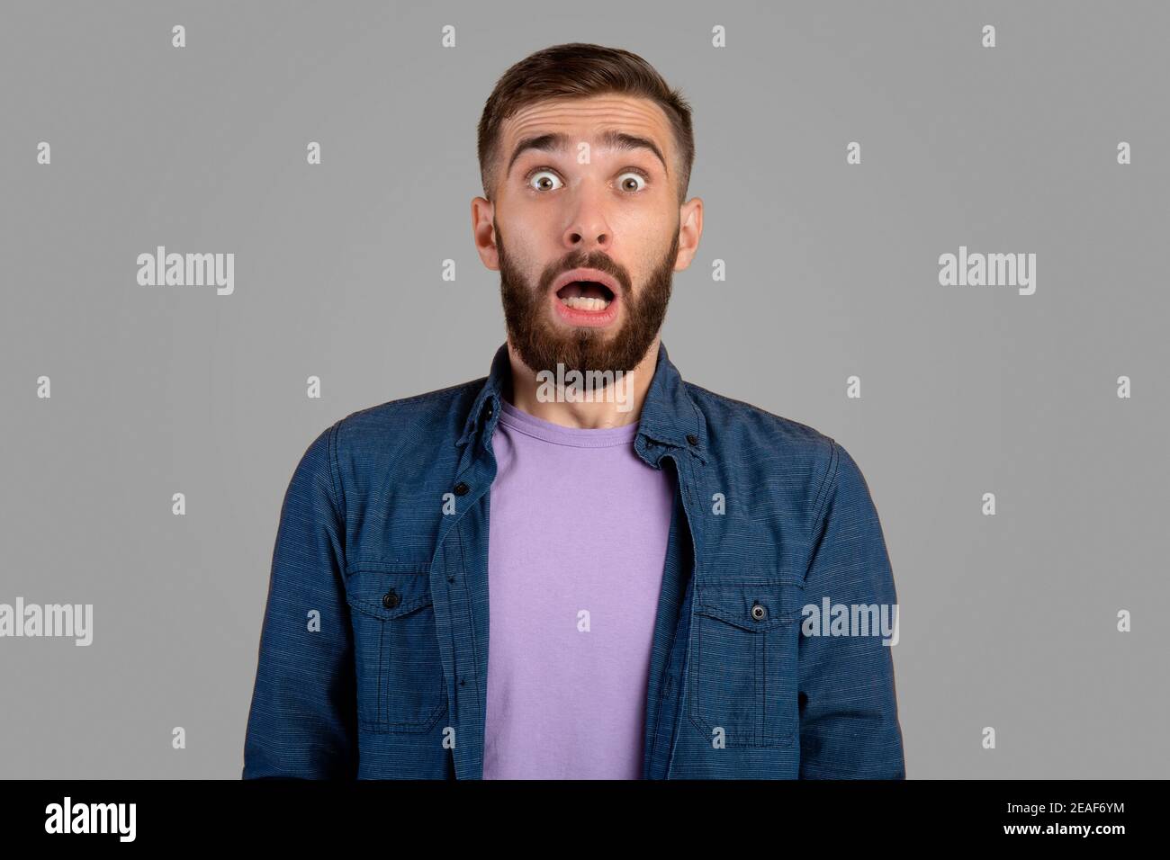 Shocked bearded guy looking at camera in panic over grey studio background Stock Photo