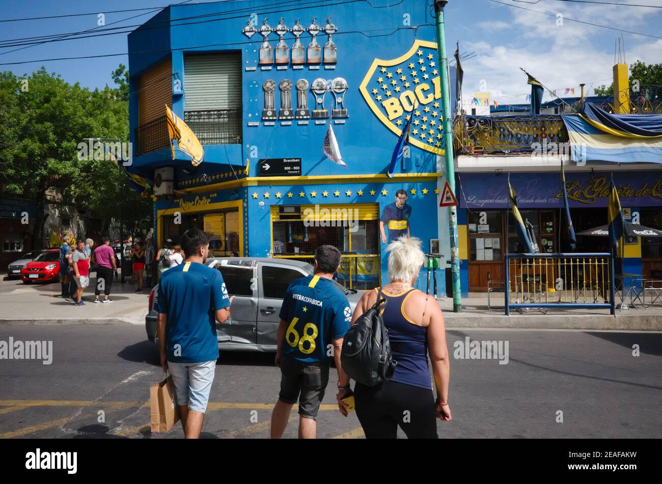 Buenos Aires, Argentina - January, 2020: Football fans of Boca Juniors club crossing road near La Bombonera stadium and fan shop in front of it Stock Photo