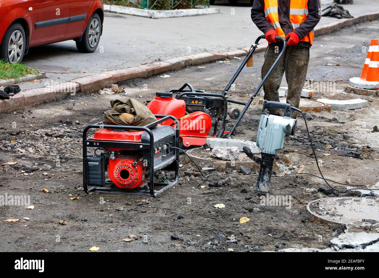 A road worker repairs and installs sewers on the road using a compactor  plate, an electric jackhammer and a petrol generator Stock Photo - Alamy