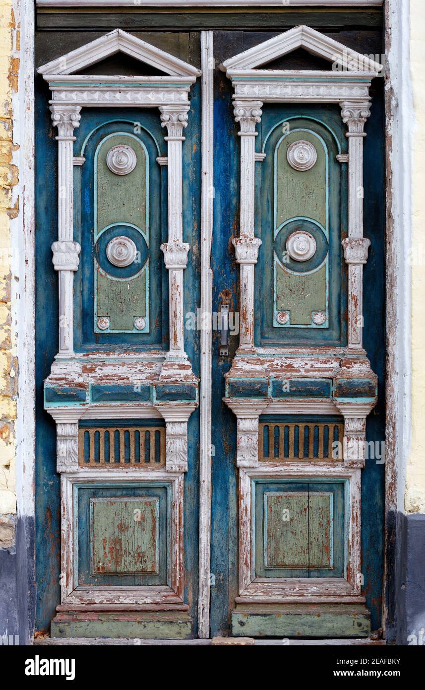 Old high wooden entrance doors in white, blue and green with carved elements frame the entrance of the old house in a carved symmetrical pattern. Stock Photo